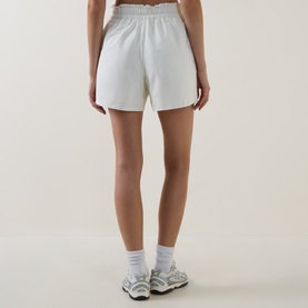 Model wearing Sweaty Betty Lily White shorts, back view, styled with white ankle socks and grey trainers.
