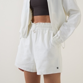 Model wearing Sweaty Betty Lily White shorts with elasticated waist, styled with matching white jacket and dark crop top.