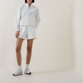 Model wearing Sweaty Betty Lily White shorts, styled with matching white overshirt, white socks and grey running trainers.