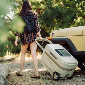 Model with Solo Stove Windchill 47 Cooler & Fan in cream, being wheeled outdoors beside a vintage vehicle in a wooded setting