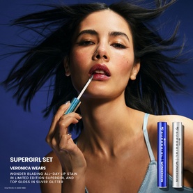 Model wearing Wonderskin Supergirl Set lip stain and gloss in silver glitter, shown alongside two product tubes on blue background