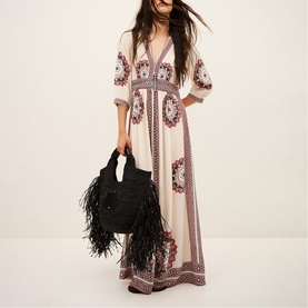 Model wearing Bash cream maxi dress with floral embroidery and V-neckline, carrying black feather-trimmed bag