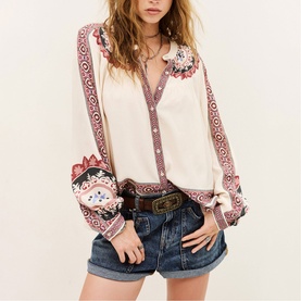 Model wearing Bash cream blouse with boho floral embroidery, V-neck and long sleeves, styled with denim shorts and brown belt.