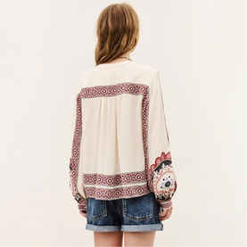 Model wearing Bash cream blouse with red geometric embroidery, styled with denim shorts and a novelty round mini bag.