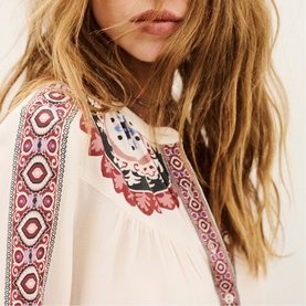 Model wearing Bash cream blouse with vibrant red and pink geometric embroidery detail on shoulders and neckline