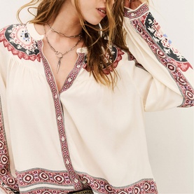 Model wearing Bash cream blouse with pink and dark floral paisley embroidered trim, V-neckline, and long sleeves, styled with a silver necklace
