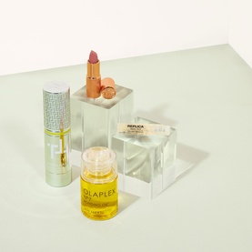 Brown Thomas gift selection featuring a lipstick, Olaplex hair oil, and Replica fragrance displayed on clear acrylic stands