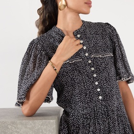 Model with Coach Hinge Bangle Bracelet in shiny gold-tone brass with cubic zirconia, worn on wrist, styled with black floral dress