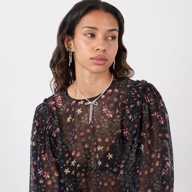Model with Coach Bow Pearl Drop Stud Earrings in pearl and gold, featuring bow motif and pearl drops, styled with floral blouse and necklace