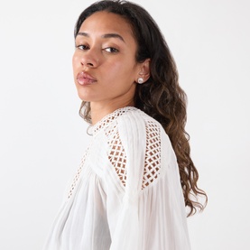 Model with Coach Logo Pearl Stud Earrings in pearl and gold tone, featuring C logo detail, worn with white broderie anglaise top.