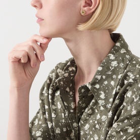 Model with Coach Logo Coin Textured Stud Earrings in shiny gold, coin motif with logo detail, styled with an olive floral shirt