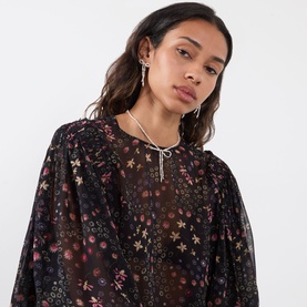 Model wearing black sheer floral and star print blouse with wide sleeves, styled with silver drop earrings and layered necklace