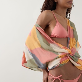 Model wearing Eres Malou Bikini Bottoms in pink with matching triangle top, styled with a multicoloured abstract print sarong tied at waist.