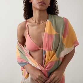 Model wearing Eres pink bikini top, styled with a multicolour abstract print sarong and gold chain necklace.