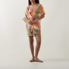 Model wearing Eres pink bikini top styled with a multicoloured abstract print sarong and flat tan sandals.