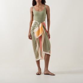 Model wearing Eres green swimsuit with a multicolour sarong wrap skirt in orange and cream, styled with flat sandals