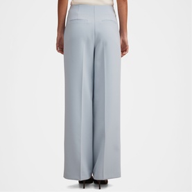 Model wearing Forever New sky blue wide-leg trousers, shown from behind, styled with a cream top and black heels.