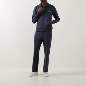 Model wearing Les Deux India Ink Blue casual zip-up track jacket, styled with matching navy track trousers and white trainers.