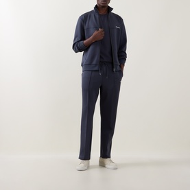 Model wearing Les Deux India Ink Blue casual zip-up jacket, styled with matching navy joggers and white trainers.