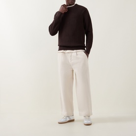 Model wearing Les Deux Mole Brown cotton crew neck sweater, styled with cream wide-leg trousers and white trainers.