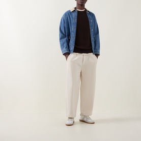 Model wearing Les Deux Mole Brown cotton crew neck knit, styled with blue denim overshirt, cream wide-leg trousers and grey trainers.