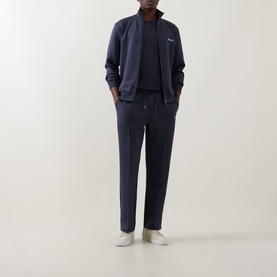 Model wearing Les Deux India Ink Blue sweatpants in polyester-elastane, styled with matching zip-up sweat jacket and white trainers.