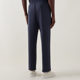 Model wearing Les Deux India Ink Blue sweatpants, rear view, tapered fit with centre crease, styled with white trainers.