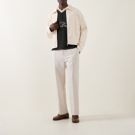 Model wearing Les Deux Rosin Green sweatshirt with cream jacket, white trousers and brown loafers.
