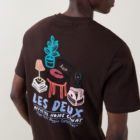 Model wearing Les Deux Record Logo Back Graphic T-Shirt in Mole Brown, showing enlarged back graphic of record player, plant and lamp illustration.