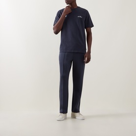 Model wearing Les Deux India Ink Blue cotton T-shirt, styled with matching navy trousers and white trainers.