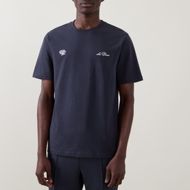 Model wearing Les Deux India Ink Blue cotton T-shirt with small chest logo embroidery, paired with matching navy trousers.