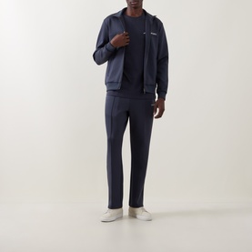 Model wearing Les Deux India Ink Blue cotton T-shirt, styled with matching zip-through jacket, tailored trousers, and white trainers.