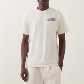 Model wearing Les Deux ivory cotton T-shirt with small chest logo print, styled with matching ivory shorts.
