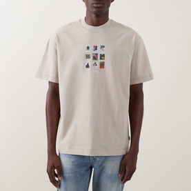 Model wearing Les Deux light sand cotton T-shirt with multicolour graphic print, styled with blue jeans.