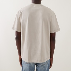 Model wearing Les Deux light sand cotton T-shirt, rear view, styled with blue denim jeans.