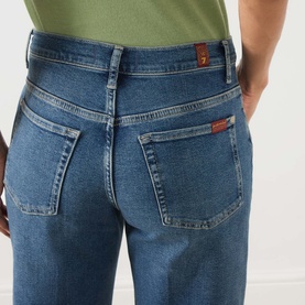 Model wearing Seven Jeans mid blue tapered jeans, close-up of back pockets and waistband detail, styled with a green top.