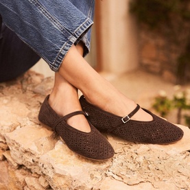 Model wearing Mint Velvet brown crochet Mary Jane flats with ankle strap, styled with blue denim jeans, on stone surface.