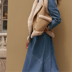 Model wearing Mint Velvet brown shearling gilet layered over a blue denim midi dress, styled outdoors