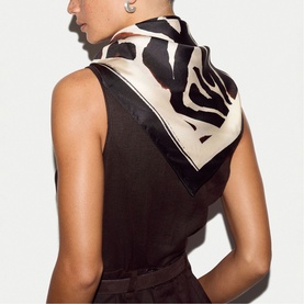 Model wearing Jigsaw cream silk scarf with black and white zebra print, tied at nape of neck over sleeveless dark top.
