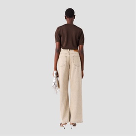 Model wearing Maje wide-leg trousers in clear beige, styled with a brown short-sleeve top and white heeled sandals, carrying a small bag.