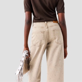Model wearing Maje clear wide-leg jeans with subtle splatter detail, styled with a brown short-sleeve top, rear view