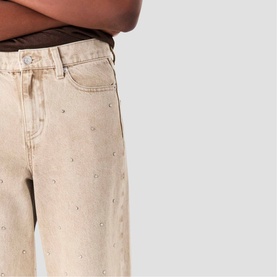 Model wearing Maje wide-leg clear denim jeans with scattered stud embellishments, cropped at hip in lifestyle shot