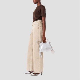 Model carrying Maje bag in clear silver metallic finish, styled with brown tee, wide-leg beige trousers and white heeled mules