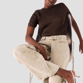 Model wearing Maje Womens French Dress in clear, seated, styled with wide-leg beige trousers and white strappy heels