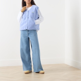 Model wearing American Vintage Hoktown Logo Gilet in Givre Chine, styled with a white long-sleeve top and wide-leg light-wash jeans