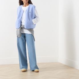 Model wearing American Vintage Hoktown Logo Gilet in Givre Chine fleece, styled with white tee and wide-leg light blue jeans.