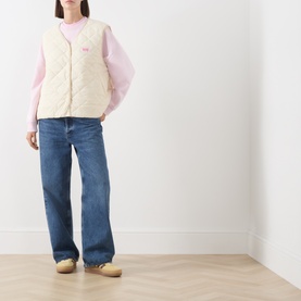 Model wearing American Vintage cream quilted gilet over pink long-sleeve top, styled with blue wide-leg jeans and tan loafers