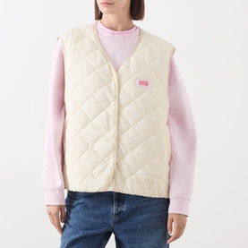 Model wearing American Vintage cream quilted gilet with V-neckline and logo patch, styled with pink long-sleeve top and blue jeans.