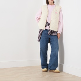 Model wearing American Vintage cream sherpa gilet over pink sweatshirt, styled with blue wide-leg jeans and striped shirt tied at waist.