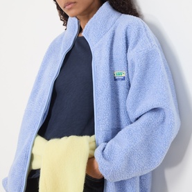 Model wearing American Vintage Hoktown Logo Fleece Jacket in Givre Chine, styled with a navy top and yellow skirt